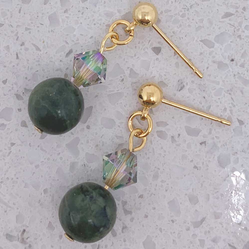 A pair of gold-plated green jade and crystal drop earrings with butterfly clips on a white surface.